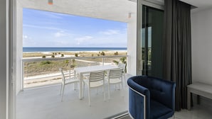 A balcony with a white table and chairs, a blue armchair, and a view of the beach and ocean.