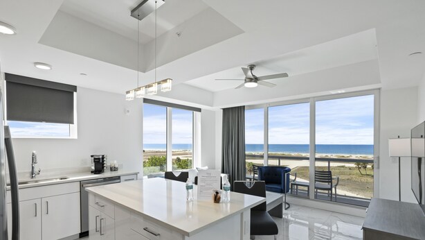 A modern kitchen with a large island, white cabinetry, and a view of the beach.