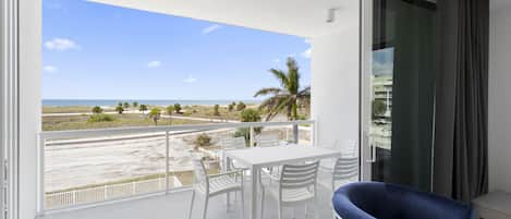 A balcony with a white table and chairs, a blue chair, and a view of the beach and ocean.