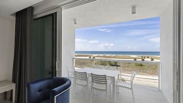 Ein Balkon mit weißem Tisch und Stühlen, einem blauen Sessel und Blick auf den Strand.