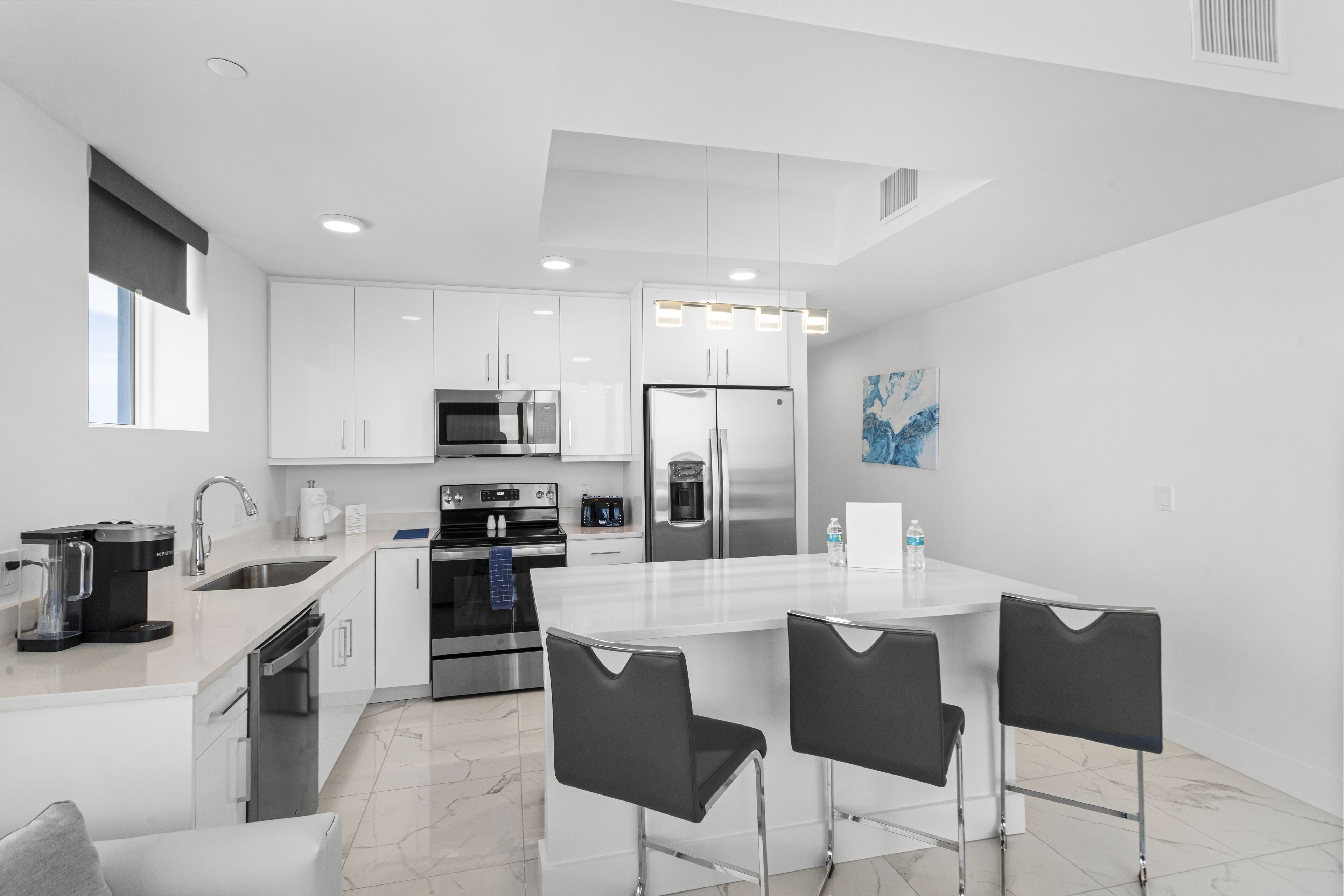 A modern kitchen with white cabinetry, stainless steel appliances, and a central island with bar stools.