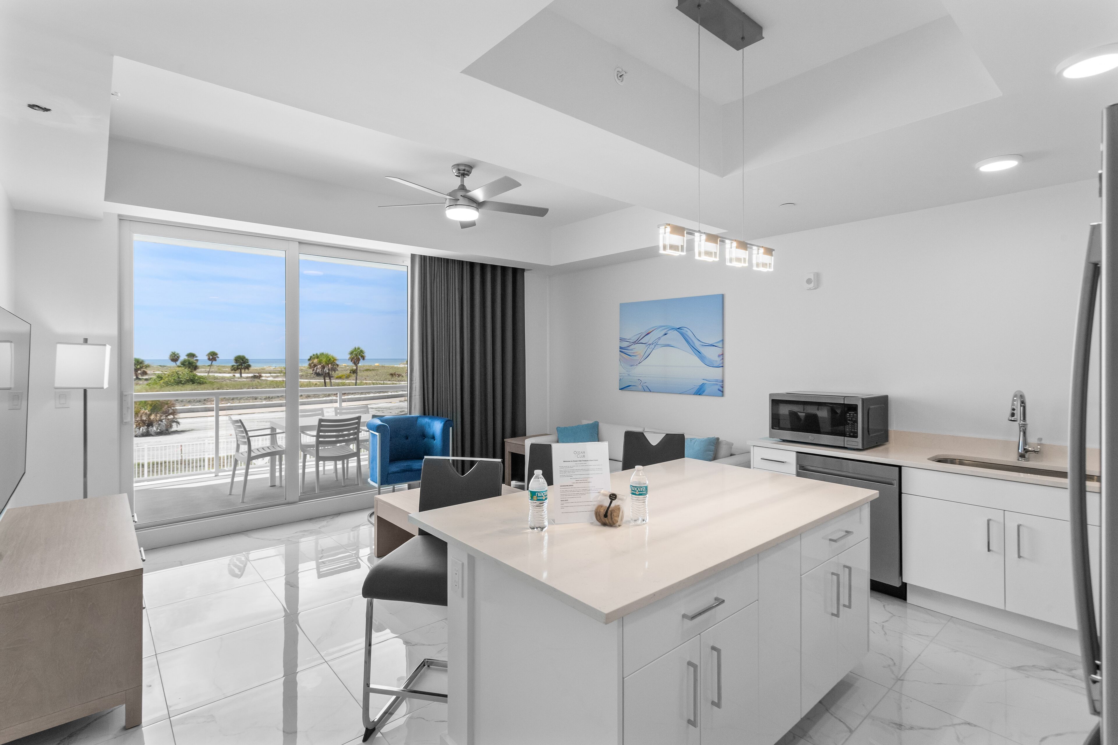 Una cocina moderna con una isla grande, un comedor con sillas, un ventilador de techo y vistas al exterior.