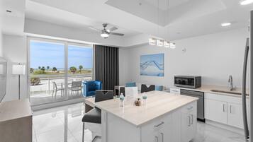 Una cocina moderna con una isla grande, un comedor con sillas, un ventilador de techo y vistas al exterior.