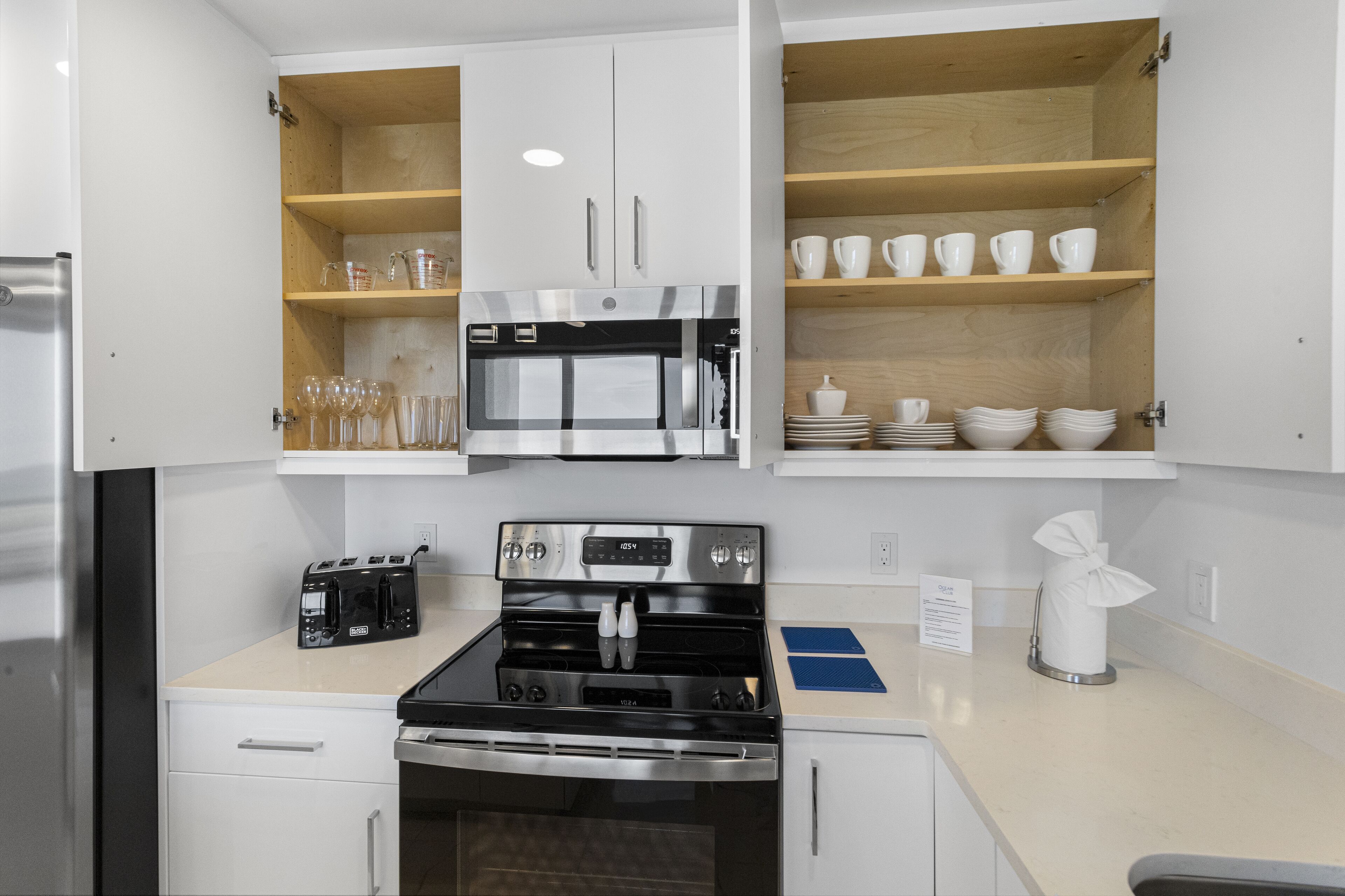Una cocina con gabinetes blancos, horno de acero inoxidable, microondas y tostadora.