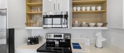 Una cocina con gabinetes blancos, horno de acero inoxidable, microondas y tostadora.