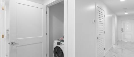 Un pasillo limpio y moderno con puertas blancas y una lavadora en una esquina.