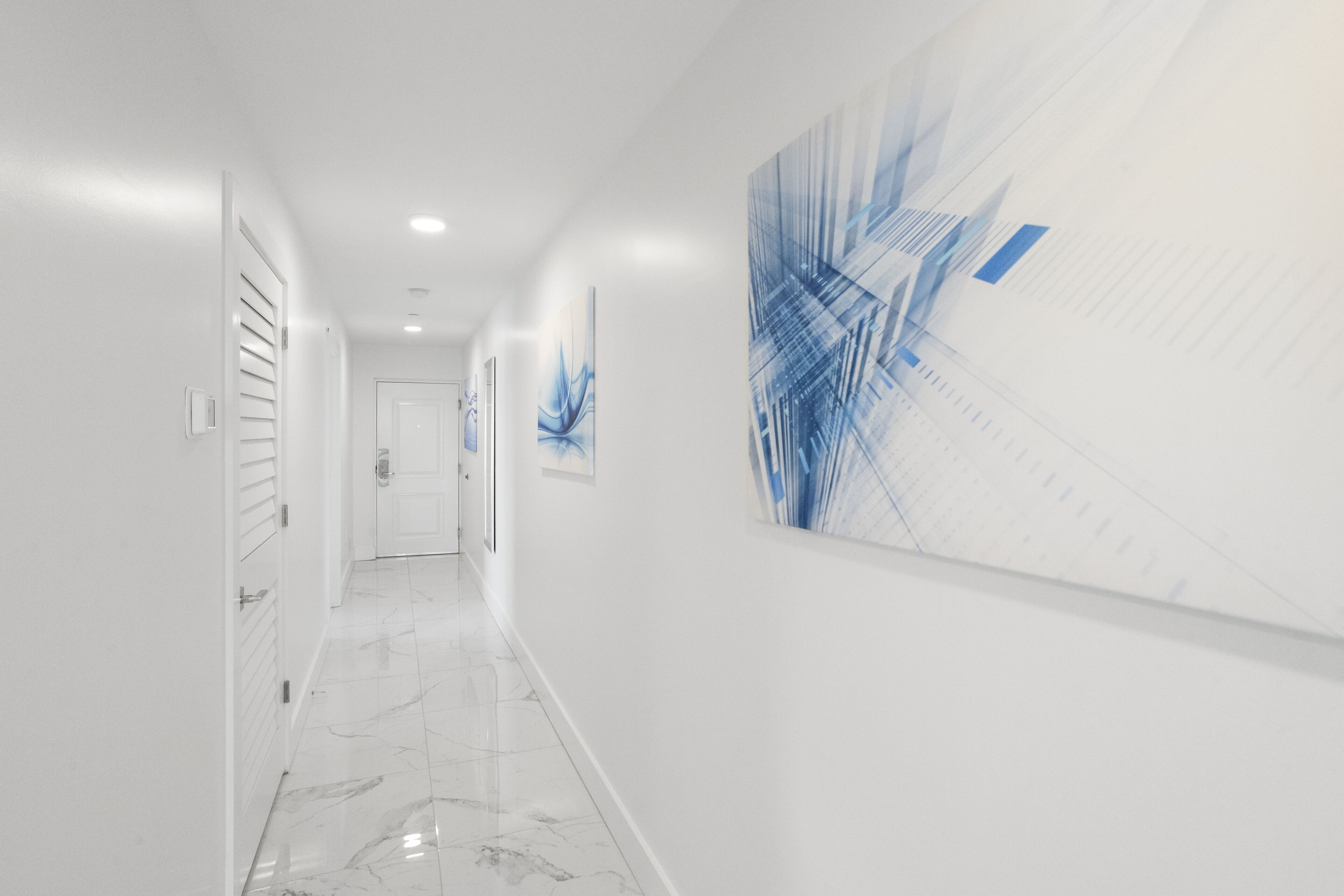 A hallway with white walls, a marble floor, and a large abstract blue painting on the right.