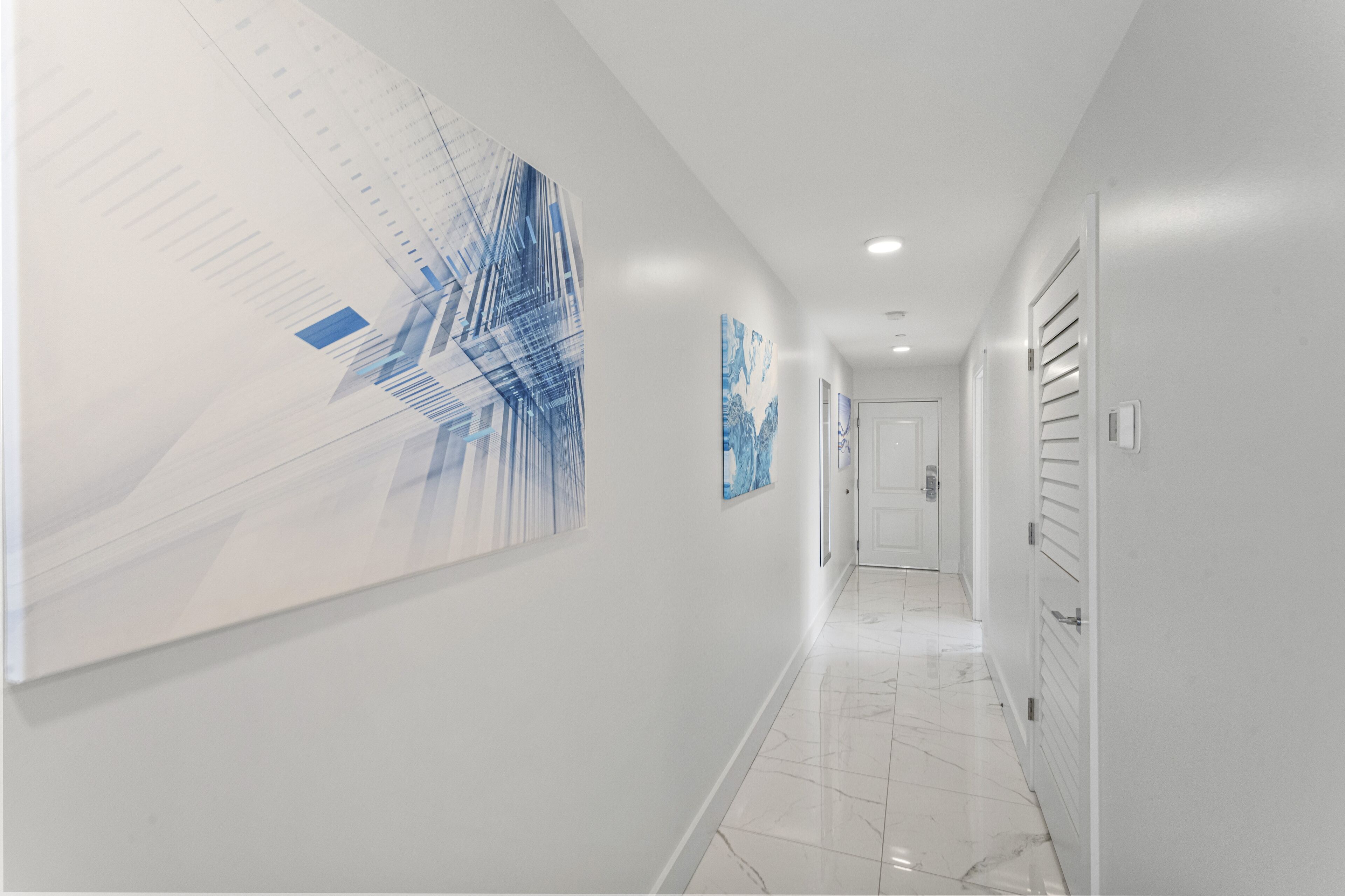 A modern hallway with a large abstract painting on the left, a door at the end, and a white tiled floor.