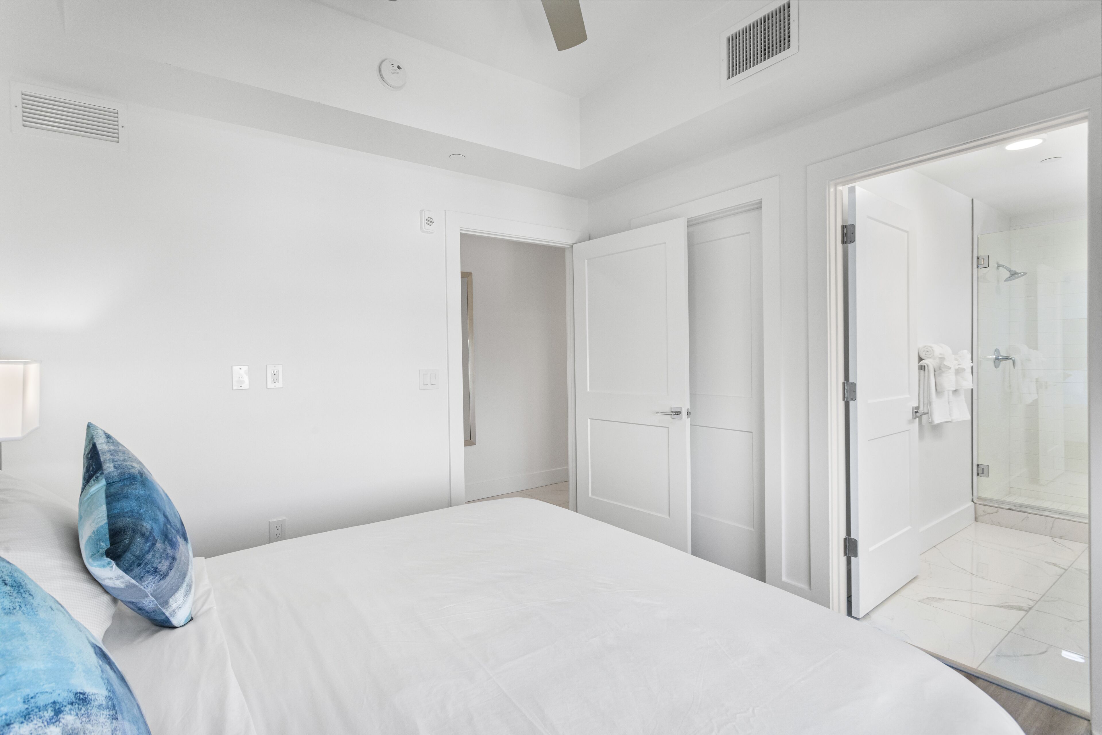 Moderni hotellihuone, jossa on suuri sänky, erillinen vaatehuone ja lasiseinäinen suihkutila.