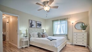 A bedroom with a bed, bedside tables, a dresser, a ceiling fan, and a window with curtains.