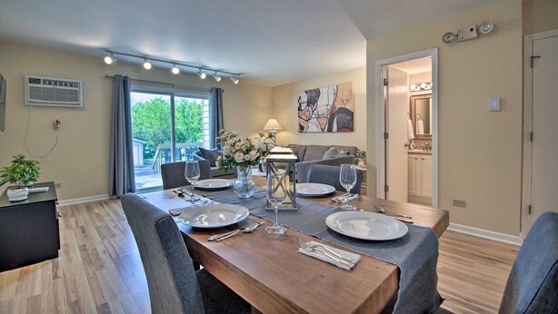 A dining area with a wooden table set for four, a vase of flowers, and a painting on the wall.