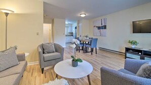 A modern living room with a grey sofa, a round coffee table, and a dining area with a table and chairs.
