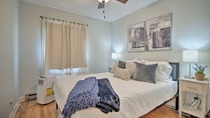 Une chambre à coucher comprenant un lit, un ventilateur de plafond, une fenêtre avec des rideaux et deux lampes fixées au mur.