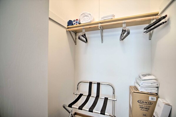 A laundry area with a metal rack, a shelf with folded towels, and a box labeled 'GRACO PACK 'N PLAY'.
