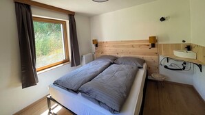 Een slaapkamer met een houten hoofdbord, een enkel bed, een nachtkastje met een lamp, een raam met gordijnen en een radiator.
