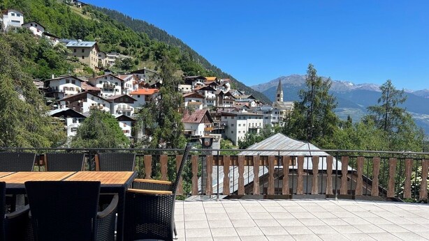 Een terras met tuinmeubilair, uitzicht op een heuveldorp en een kerktoren in de verte.