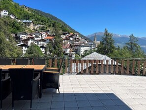 Une terrasse avec des meubles d’extérieur, une vue sur un village perché sur une colline et, au loin, le clocher d’une église.