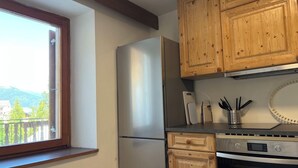 Een keuken met houten kastjes, een roestvrijstalen koelkast, een oven en een raam met uitzicht op een balkon.