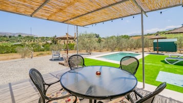 Relax by the pool under a shaded pergola, surrounded by lush greenery and a serene hillside view.