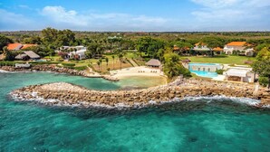 Ein Küstenort mit klarem türkisblauem Meer, einer felsigen Insel und einem Sandstrand mit Liegestühlen.