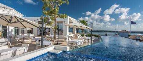A poolside area with lounge chairs and umbrellas, a clear sky, and a flag.