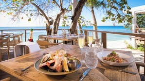 Una mesa de madera con platos de mariscos, una botella de champán y vasos de agua en un restaurante frente al mar.