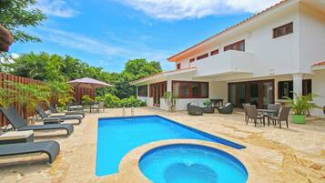A swimming pool with lounge chairs, a hot tub, and outdoor furniture.
