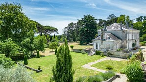 Un grand bâtiment historique en pierre, doté d’une façade symétrique, entouré de jardins bien entretenus et d’arbres imposants.
