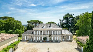 Un grand bâtiment historique en pierre, doté d’une façade symétrique, de nombreuses fenêtres et d’une cour centrale agrémentée d’un jardin circulaire.