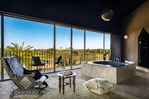 A spacious balcony with a large window, a black leather chair, a small round table with a vase, and a stone bench. - Villa Tacai - Six Bedroom Villa, Sleeps 12 (Sidi Youssef Ben Ali)
