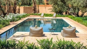A swimming pool with lounge chairs and a small table, surrounded by greenery and a building in the background. - Villa Tacai - Six Bedroom Villa, Sleeps 12 (Sidi Youssef Ben Ali)