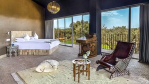 A bedroom with a large bed, a sitting area with a chair, a small table, and a view of the outdoors. - Villa Tacai - Six Bedroom Villa, Sleeps 12 (Sidi Youssef Ben Ali)