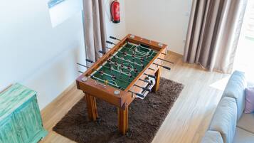 Uma mesa de futebol de bolso em um quarto com piso de madeira, um tapete macio, um armário verde e um extintor de incêndio na parede.