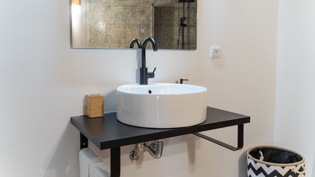 A modern bathroom with a white sink, black faucet, and a mirror above it. - Casa São José (Carvalhal)