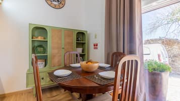 Un coin repas avec une table en bois, des chaises et un buffet vert doté d’étagères.