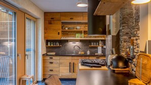 Une cuisine moderne avec des meubles en bois, un plan de travail noir et un mur d’accent en pierre.