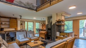 Un vaste espace de vie agrémenté de meubles en bois, d’une cheminée et de grandes fenêtres offrant une vue sur l’extérieur.