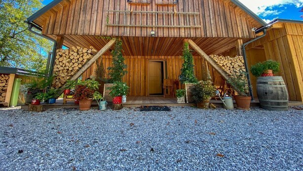 Une grange en bois dotée d’un porche, entourée de gravier et agrémentée de plantes en pot.