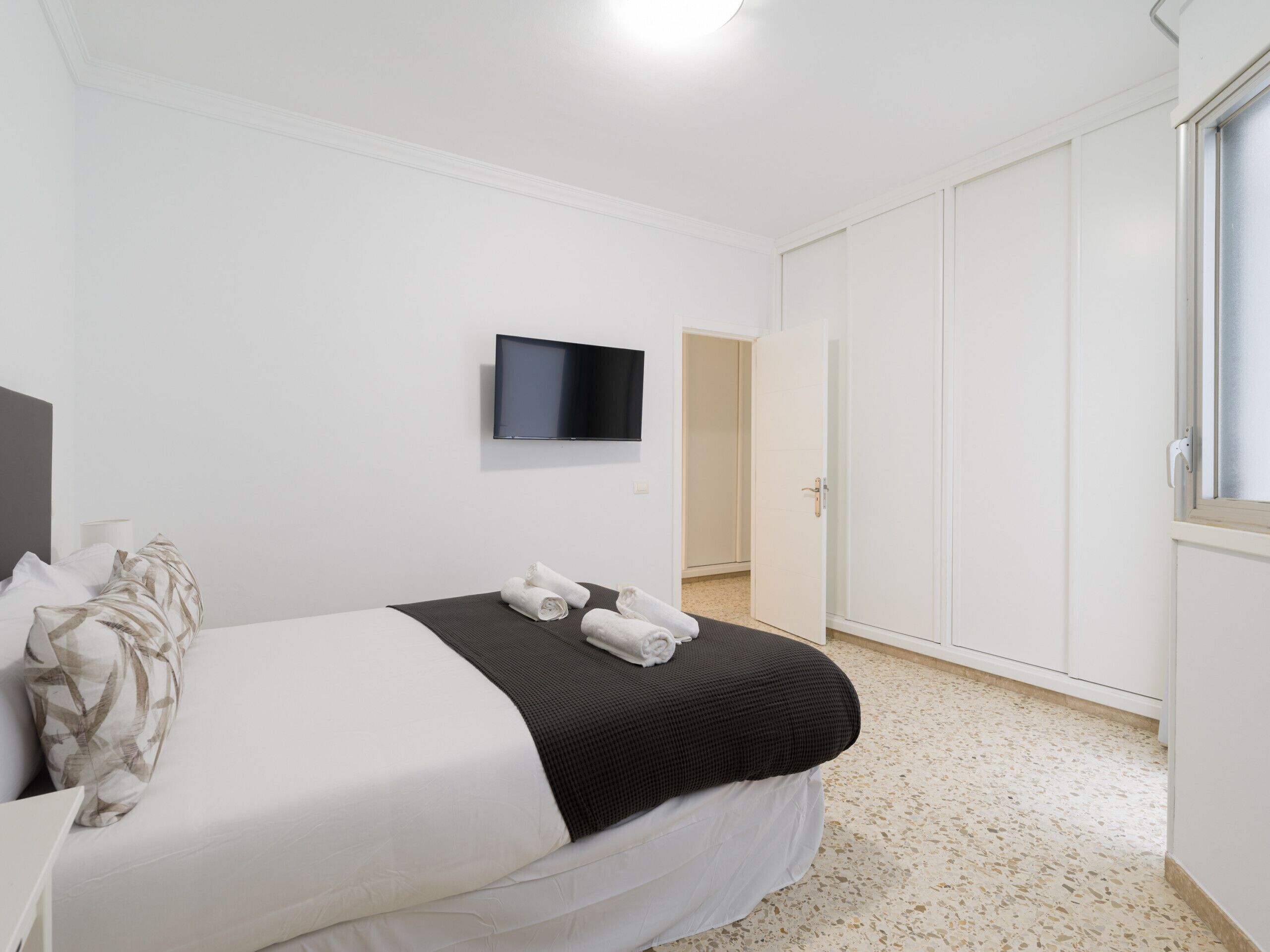 Una habitación de hotel con cama, televisor de pantalla plana en la pared y armario.