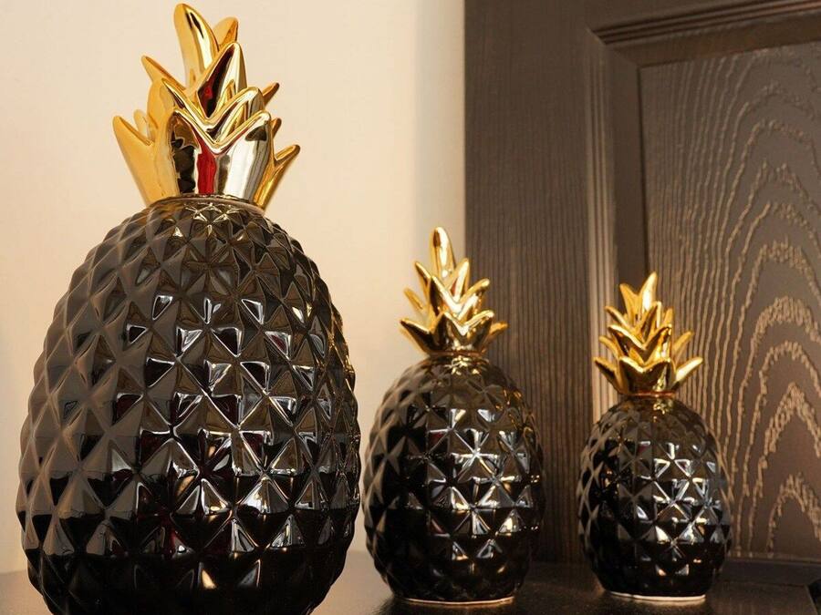 Three black, textured vases with golden pineapple tops on a dark countertop.