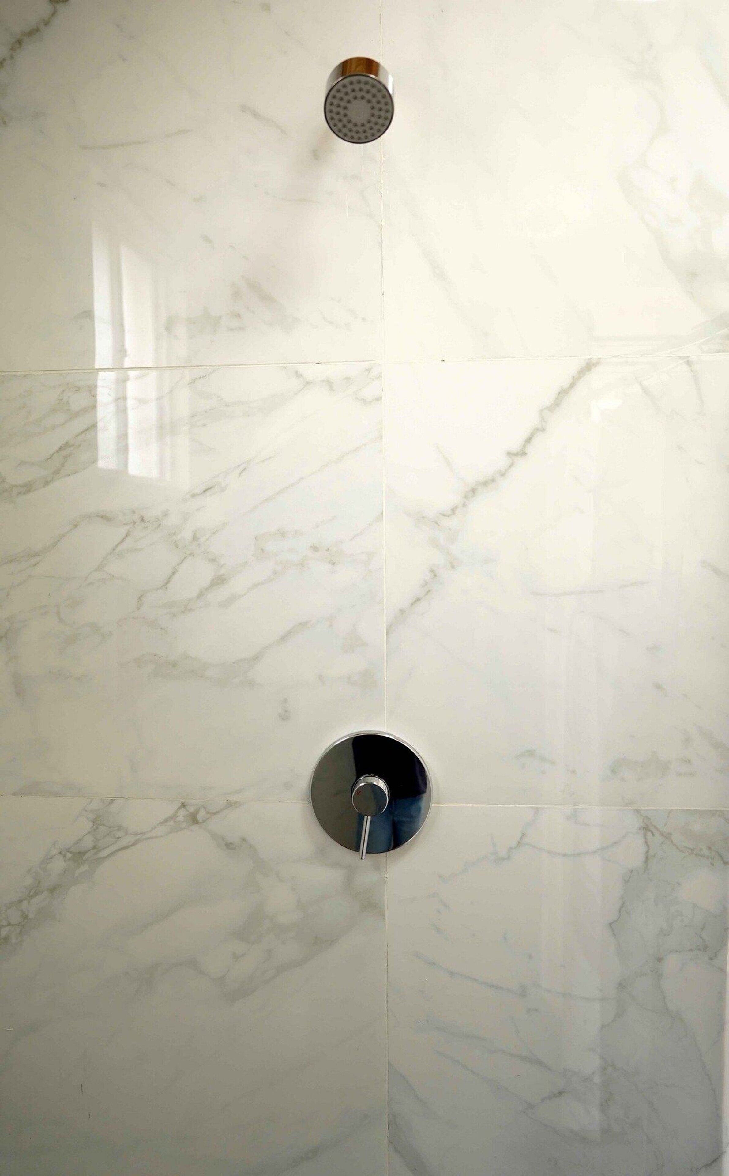 A bathroom with a marble wall, a shower head, and a faucet.