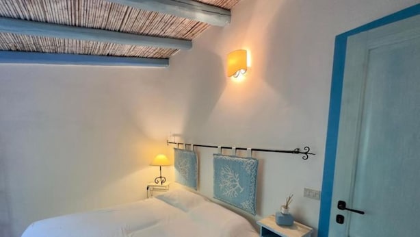 A bedroom with a bed, bedside lamp, nightstand, and a wall-mounted light fixture. - Villa Calisto - San Pantaleo (Olbia)