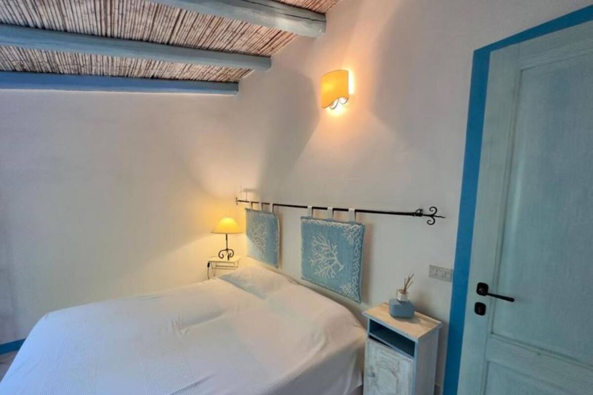 Een slaapkamer met een bed, nachtlampje, nachtkastje en een wandlamp.