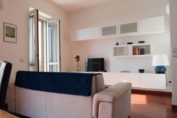 A living room with a sofa, a television, a bookshelf, and a window with curtains.