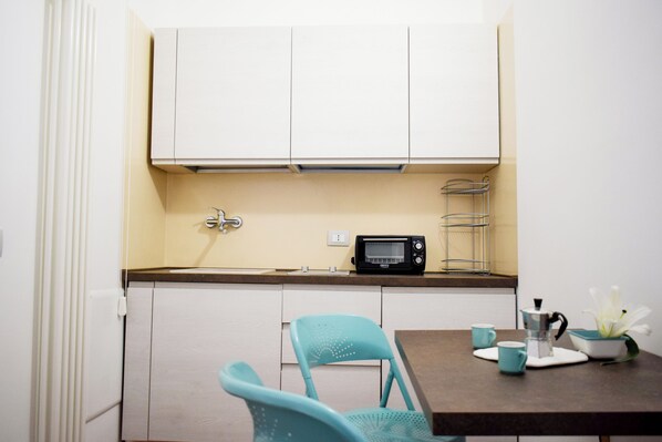 Una cocina compacta con armarios blancos, un microondas y una pequeña mesa con dos sillas.