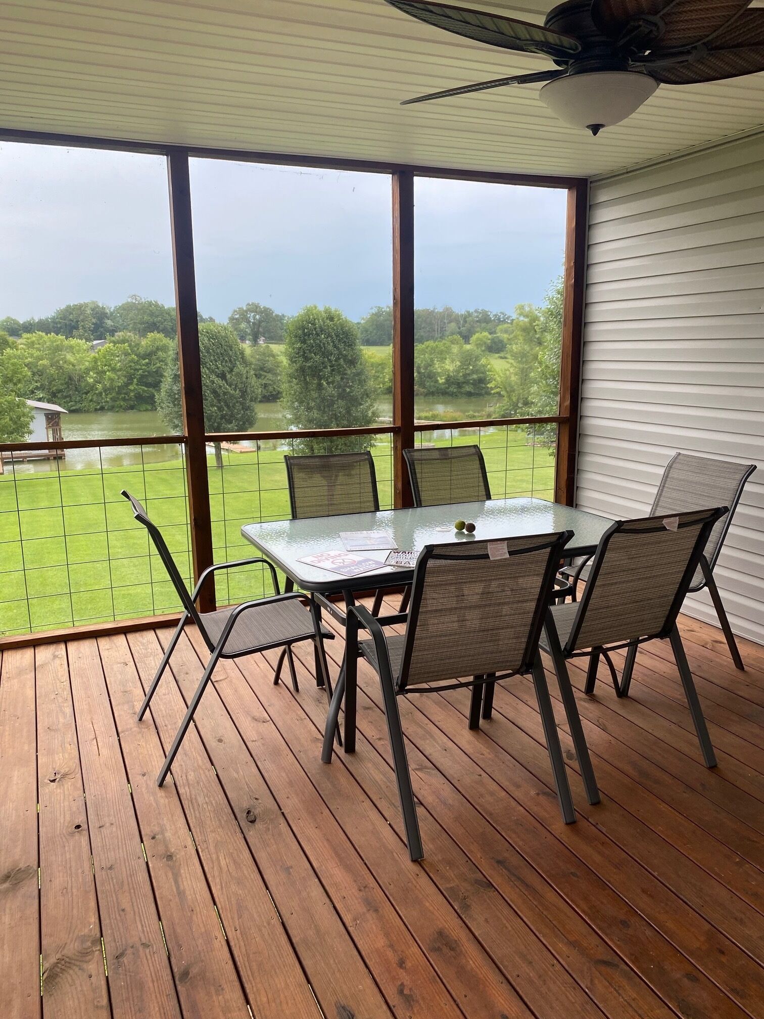 En overdækket terrasse med et bord og stole, med udsigt over en græsplæne og et vandareal.