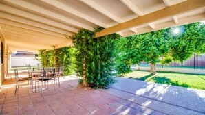 Eine überdachte Terrasse mit Fliesenboden und Metallstühlen.