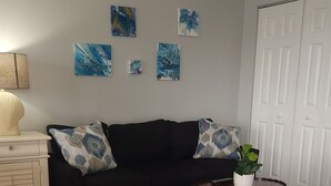Un salon avec un canapé noir, une table basse ronde, un tapis à motifs d’étoiles de mer et des œuvres d’art abstraites accrochées au mur.