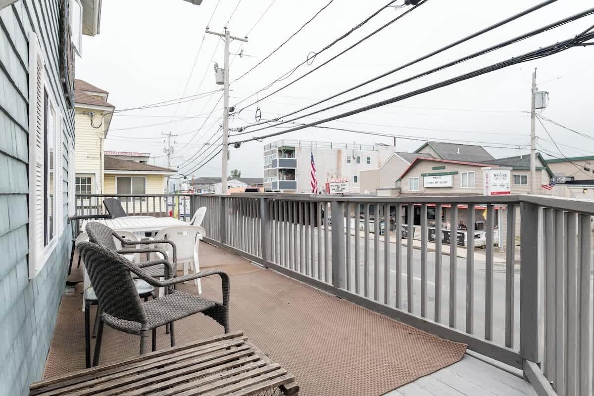 A balcony with wicker chairs and a table, overlooking a street with buildings and power lines.