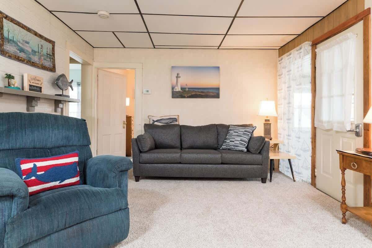 Una sala de estar con un sillón azul, un sofá gris y una lámpara sobre una mesita de madera.